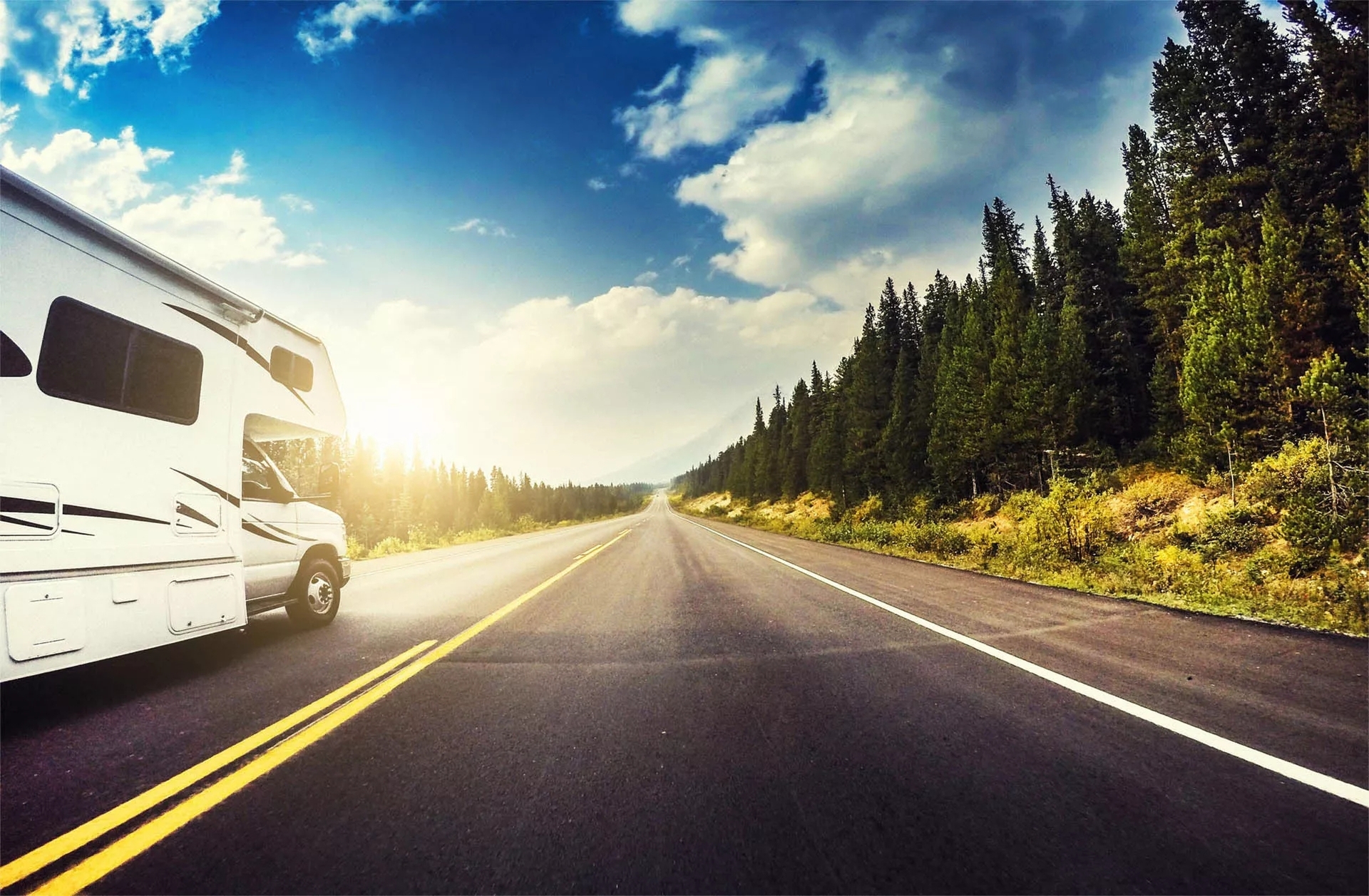 An RV heading down a road amongst vibrant trees, pavement markings, trees, and sky. An RV heading down a road amongst vibrant trees, pavement markings, trees, and sky.