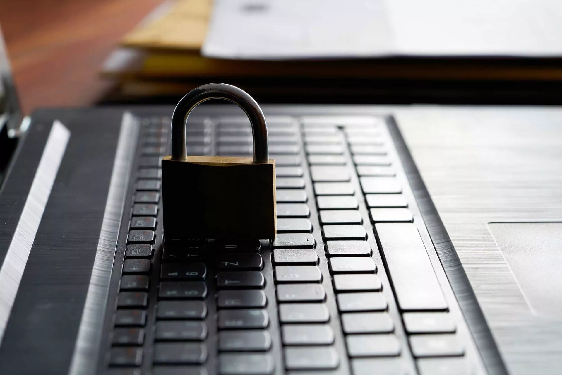 A sturdy padlock sitting on an open laptop's keyboard. The scene is viewed from the laptop's side and illuminated from behind. A sturdy padlock sitting on an open laptop's keyboard. The scene is viewed from the laptop's side and illuminated from behind.
