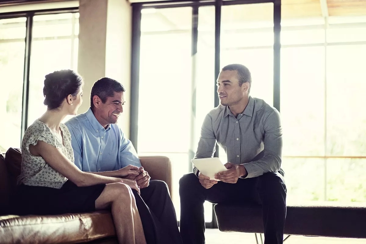 A couple in a meeting with another man with papers in his hand. They are all smiling in conversation. A couple in a meeting with another man with papers in his hand. They are all smiling in conversation.