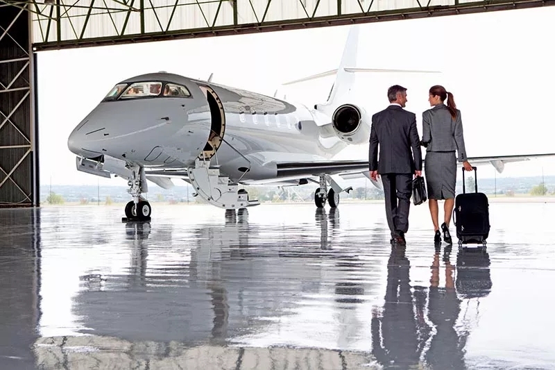 Two people walking across a hangar towards a parked aircraft.