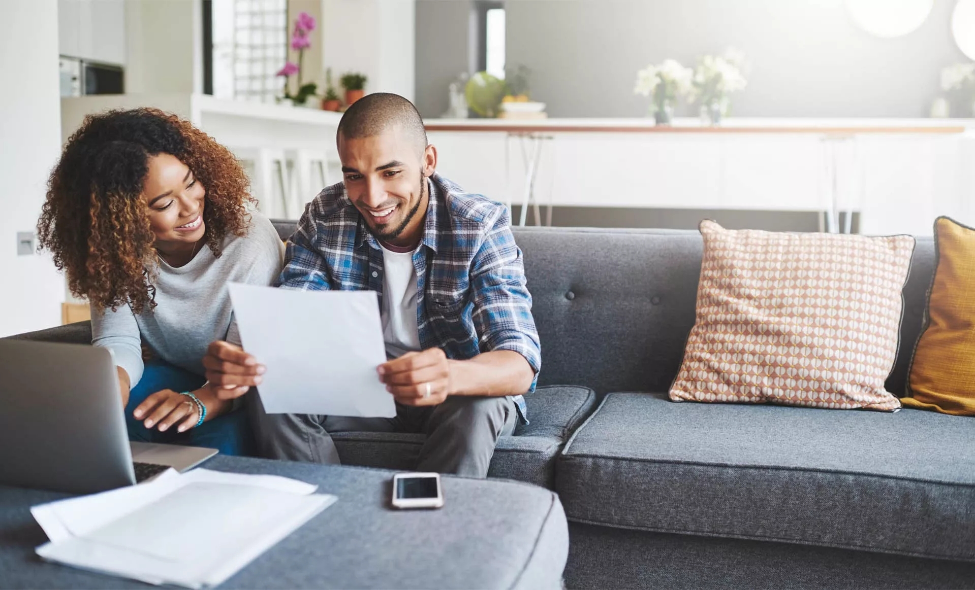 A couple sitting on their couch in the living room smiling over papers in their hands. A couple sitting on their couch in the living room smiling over papers in their hands.