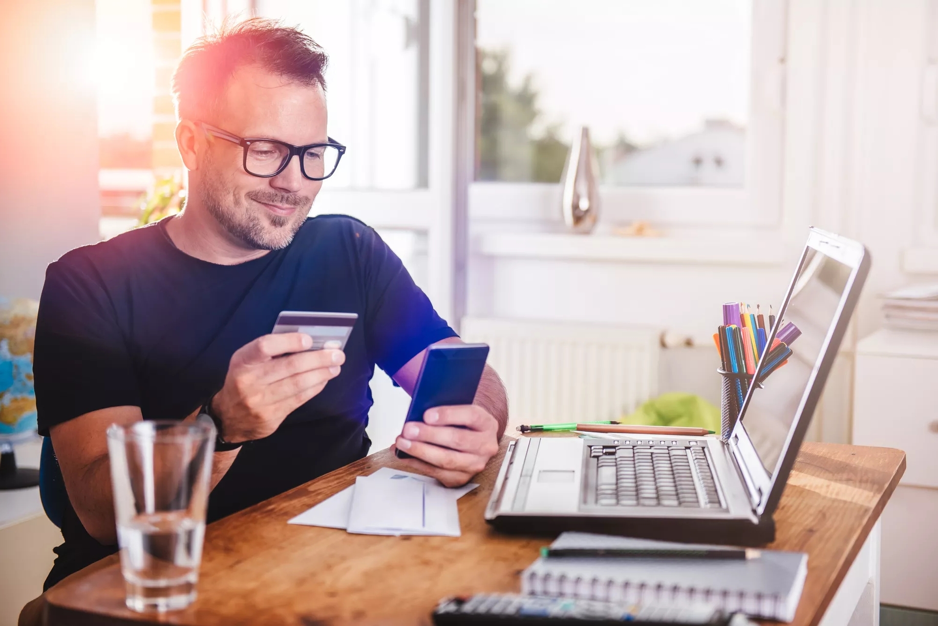 A person holding a debit card in one hand and mobile in another hand in front of a laptop. A person holding a debit card in one hand and mobile in another hand in front of a laptop.