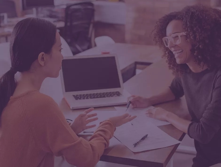 Two women discussing an open laptop on the table between them. Two women discussing an open laptop on the table between them.