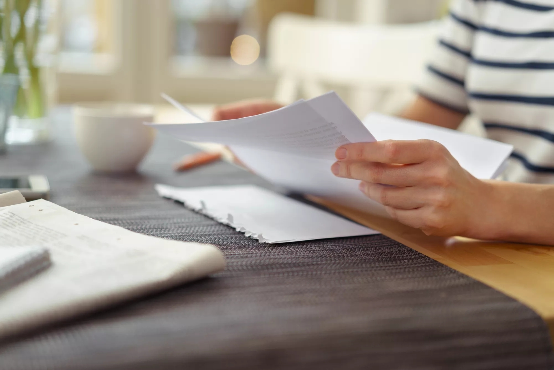 A person holding paper in their hand at a desk with more papers on it. A person holding paper in their hand at a desk with more papers on it.