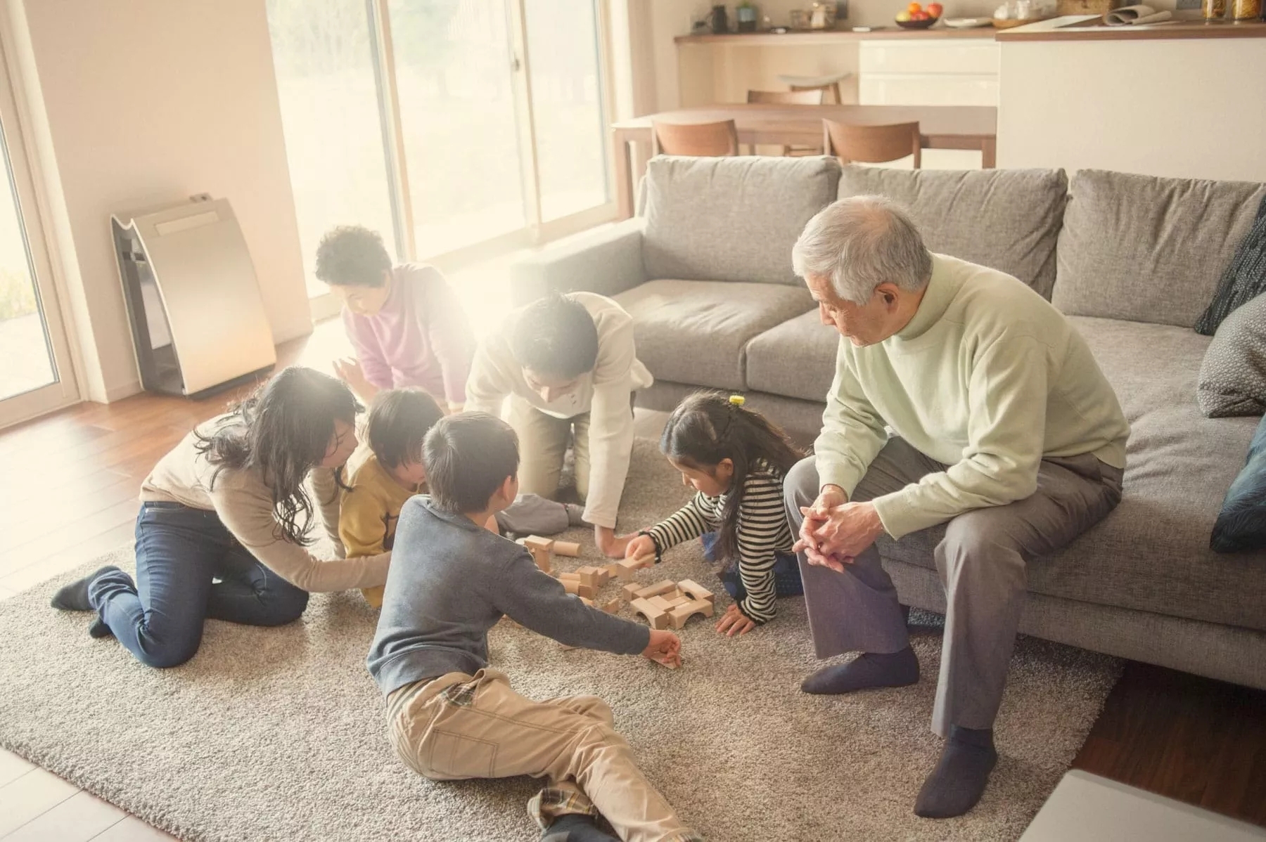 A family with three children, three adults, and two elderly people playing a board game half on the couch, half on the floor. A family with three children, three adults, and two elderly people playing a board game half on the couch, half on the floor.
