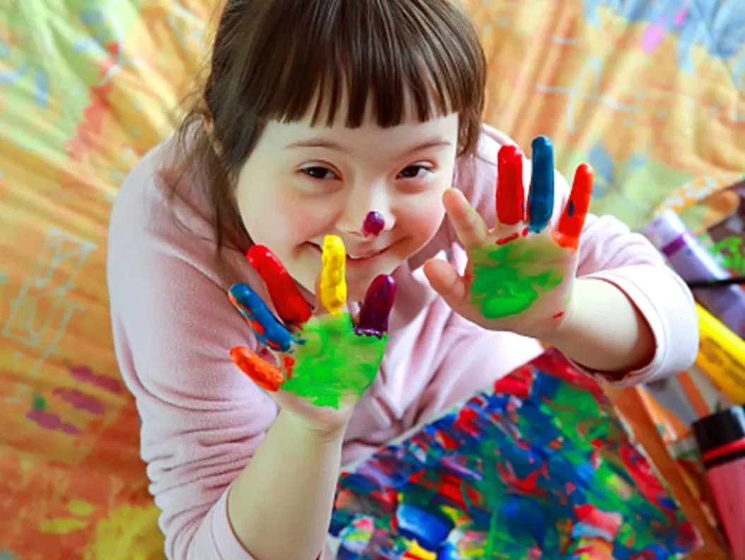 A young girl with finger paint on her hands and the art below her. A young girl with finger paint on her hands and the art below her.